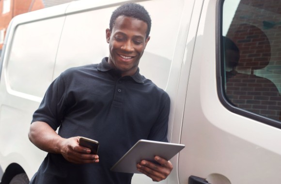 A man leaning on a work vehicle with a tablet and phone