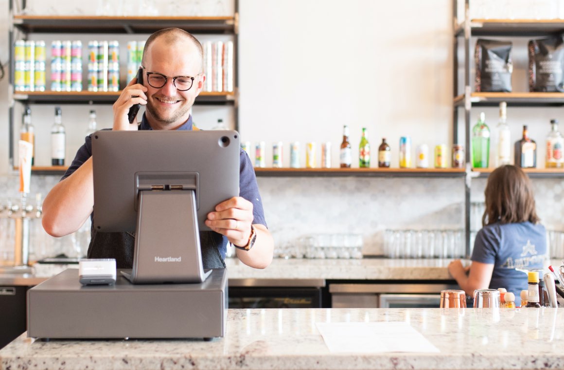 A bar worker looking at a point of sale screen while being on the phone