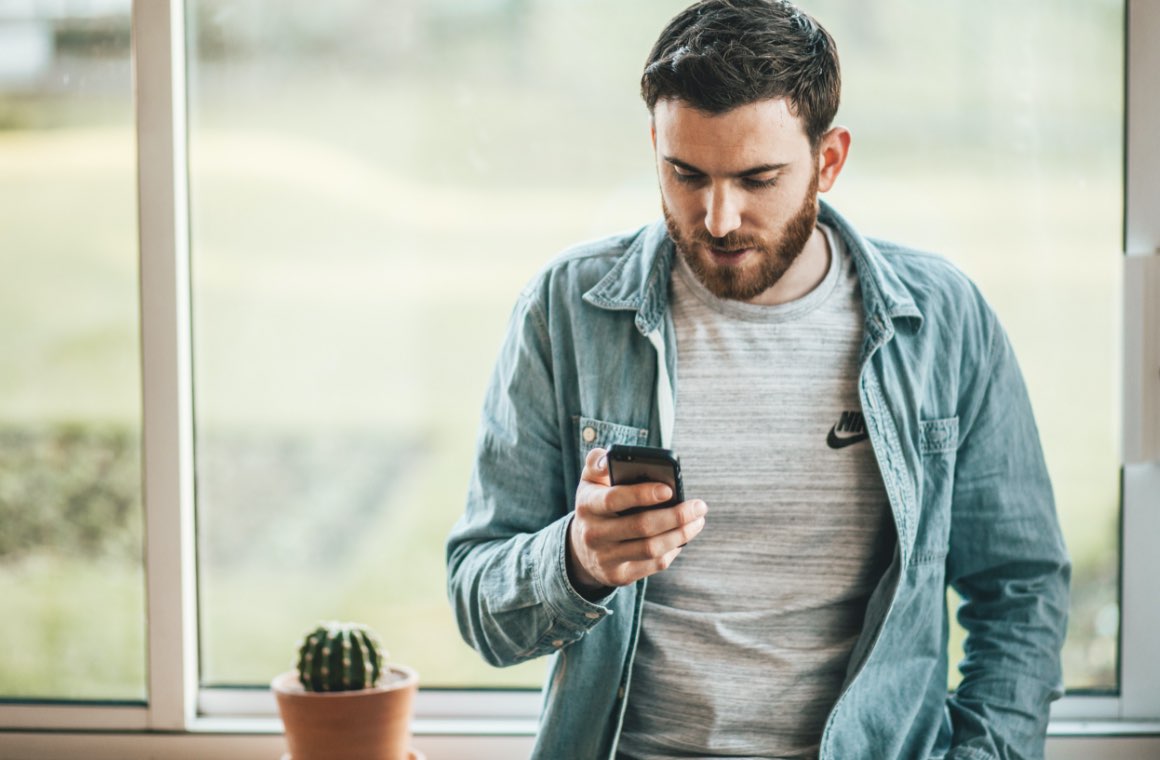 A man by a window looking at his mobile phone