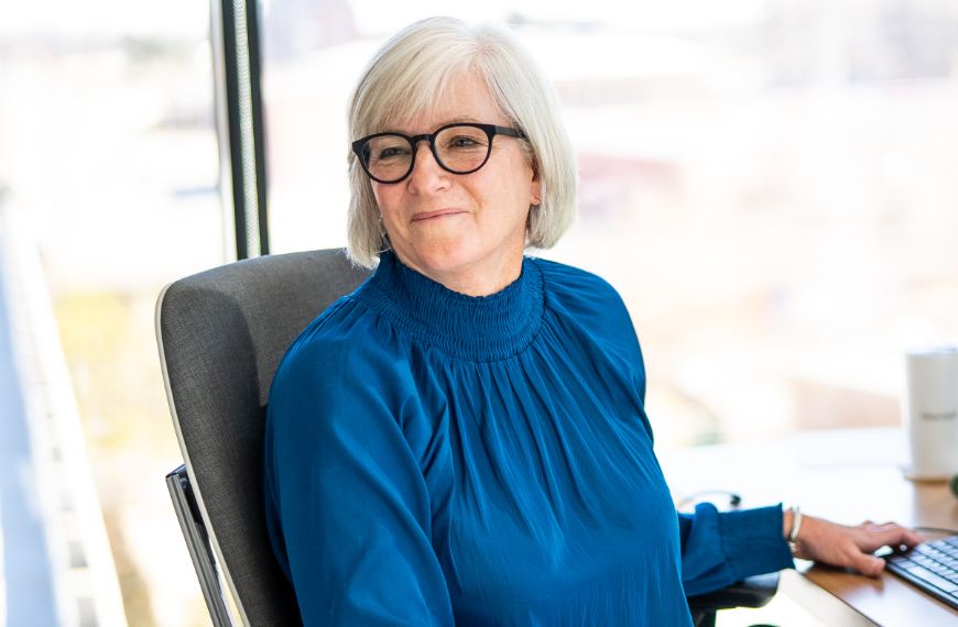 A female Heartland employee wearing glasses is sitting at her desk and smiling