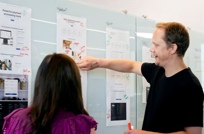 A male and female Heartland employee are pointing to website plans on a whiteboard 