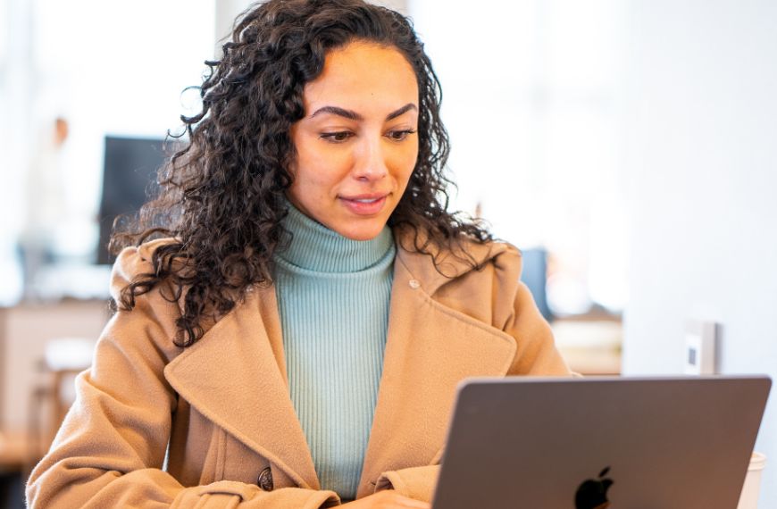 A female Heartland employee is sitting in an office, reading something on her laptop and smiling 