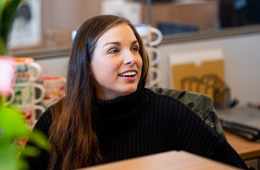 A woman smiles as she listens to someone speak at her office desk.