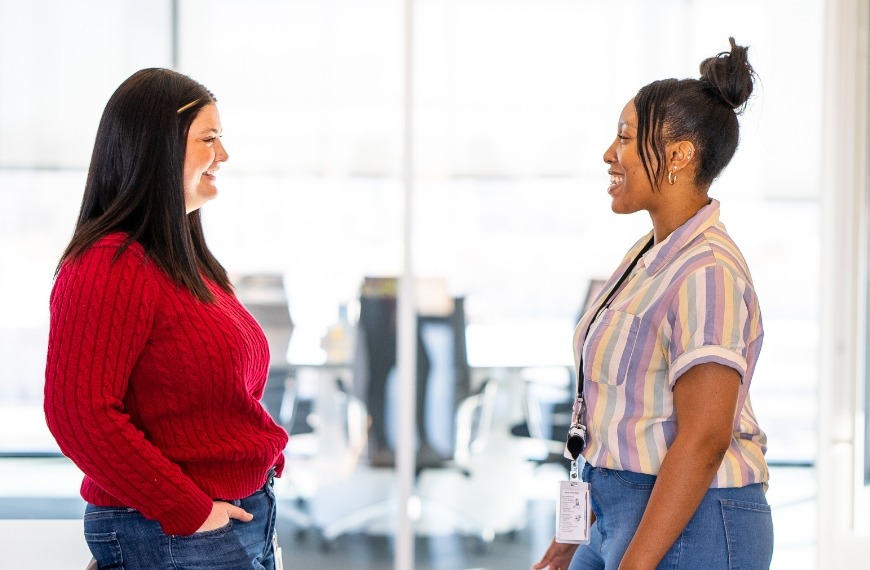 Two women face each other in conversation in an open office.