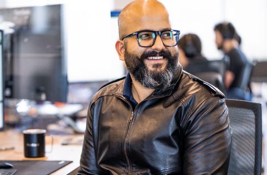 A Heartland team member wearing a leather jacket sits at his desk, smiling.