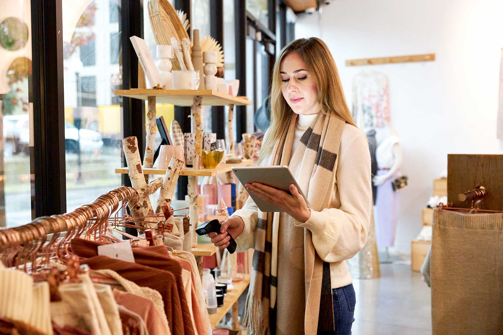 A woman is scanning clothes on a rack while holding a tablet. 