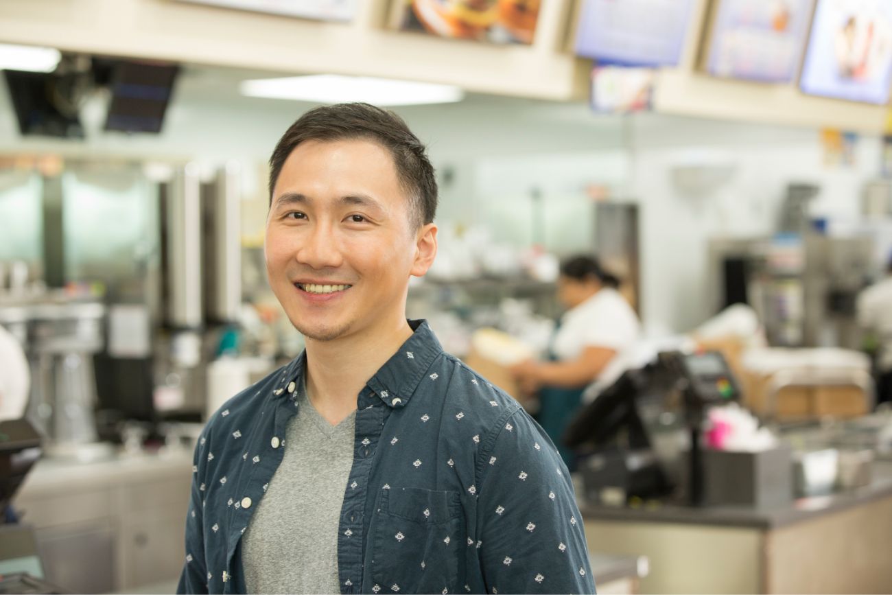 An employee standing in a restaurant kitchen smiling.