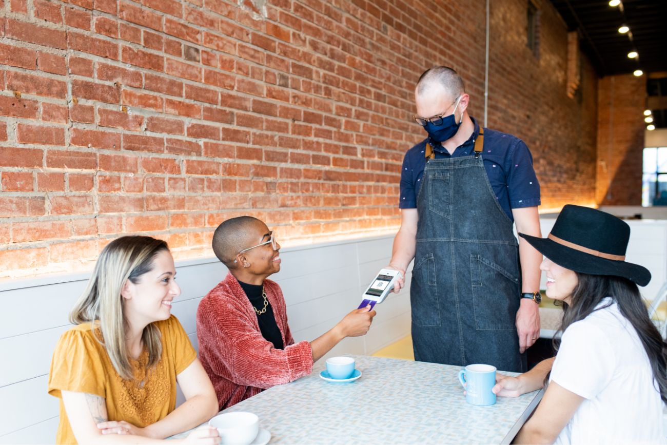 An employee using a handheld POS device to take payment from his table of customers at a restaurant.