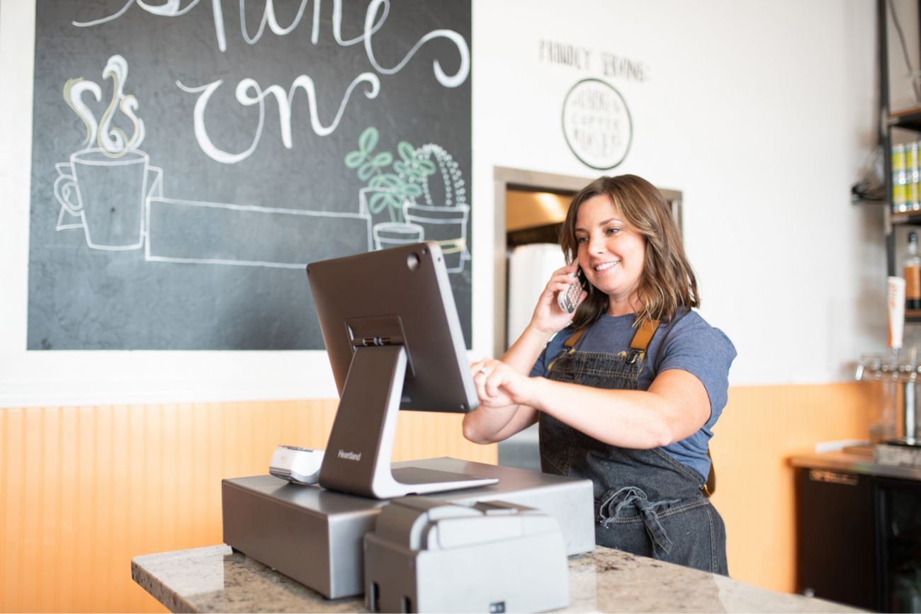 A woman standing at a POS system while talking on the phone.