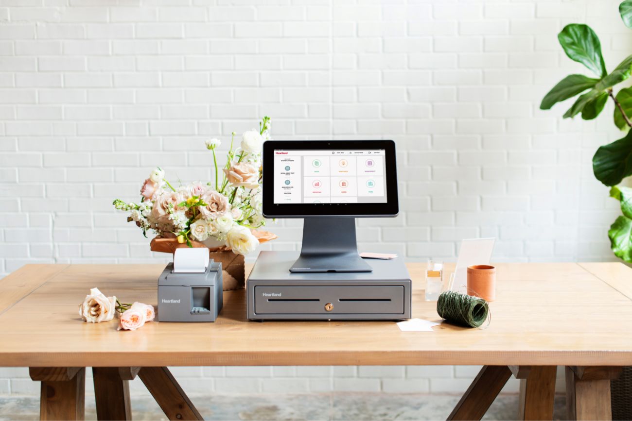 A POS system sitting on a table with a lit up screen.