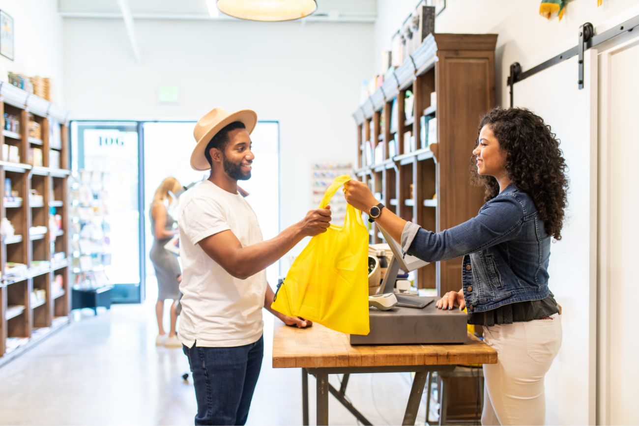 A woman handing a male shopper a bag full of purchased products.