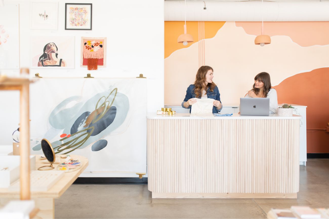 Two women standing behind a check-out counter talking in a store.