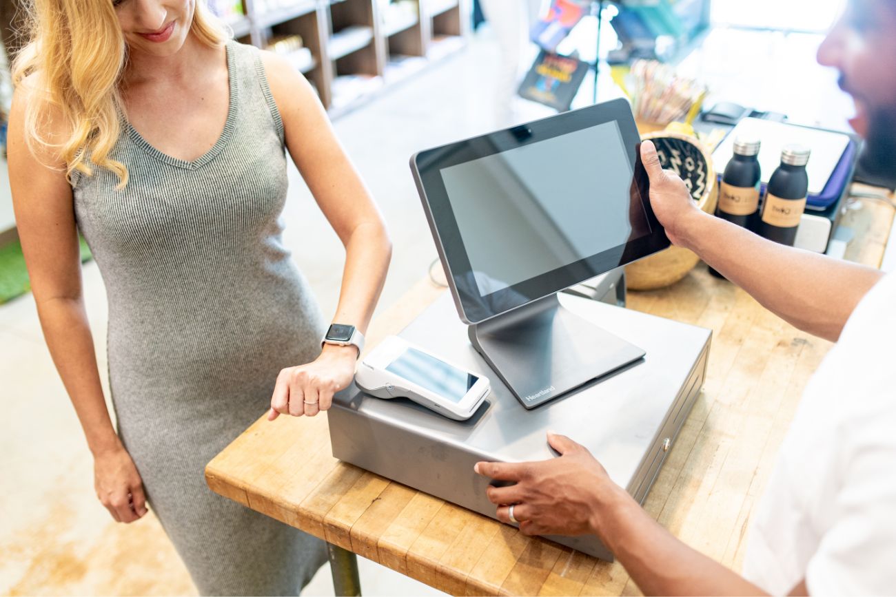A black POS screen system on a table and a woman using her smart watch to pay.