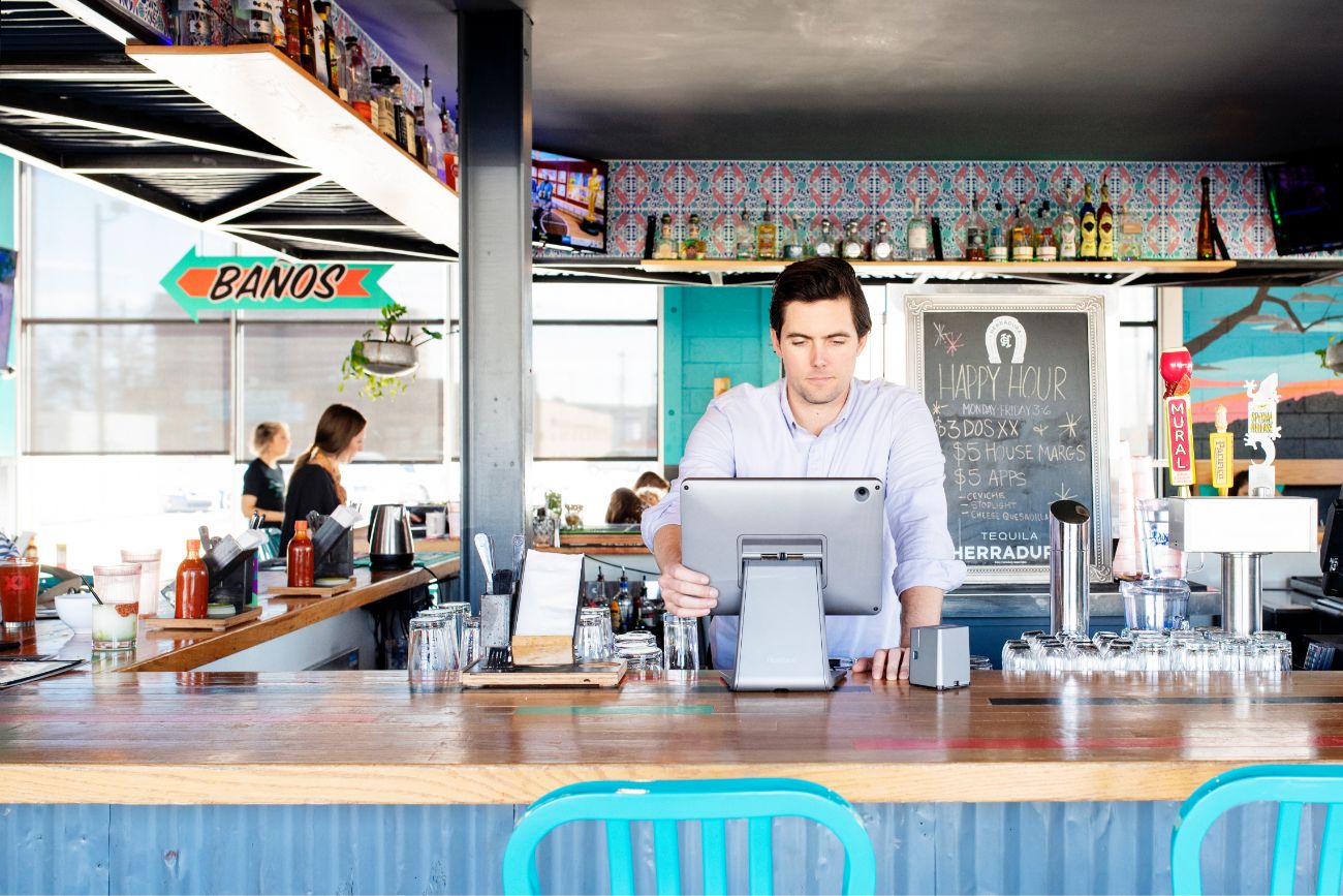 A man standing behind the counter at a restaurant looking at a POS screen.