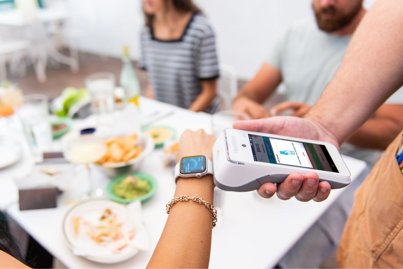 An arm with a smart watch paying at a restaurant with their watch. 