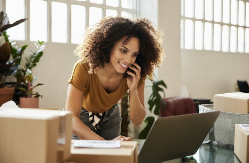 A woman talking on a phone and looking at her laptop