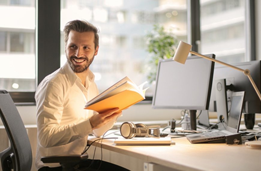 A man at a desk, holding papers and smiling