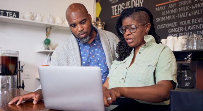 Two small business owners discussing information while looking at a laptop together.