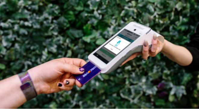 A closeup of a hand inserting a card into a payment device held by another person.