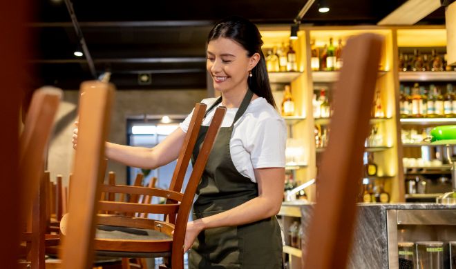 Female restaurant employee putting chairs on tables at end of day