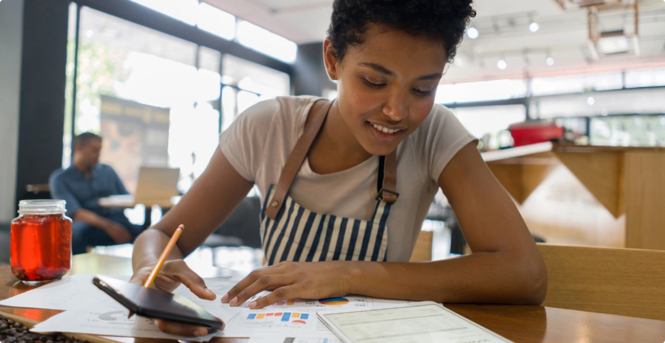 Woman in restaurant setting going over merchant data using her mobile device