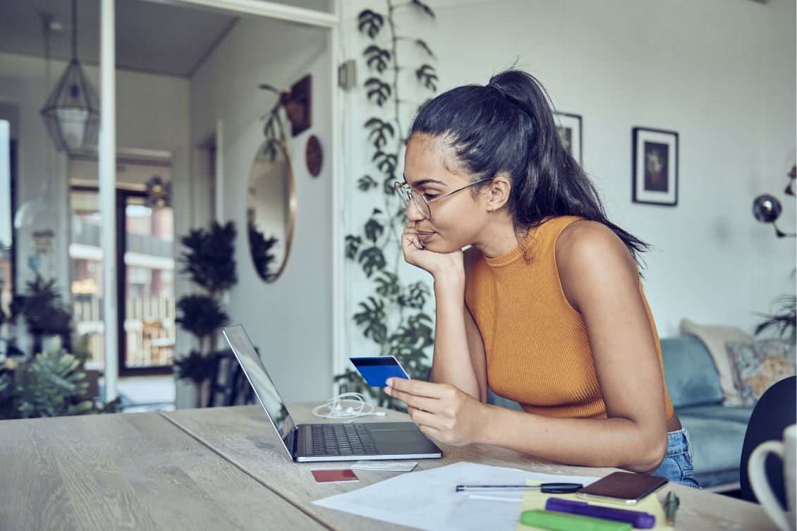 A woman sitting at a desk looking at her laptop and holding a credit card to submit a small business chargeback