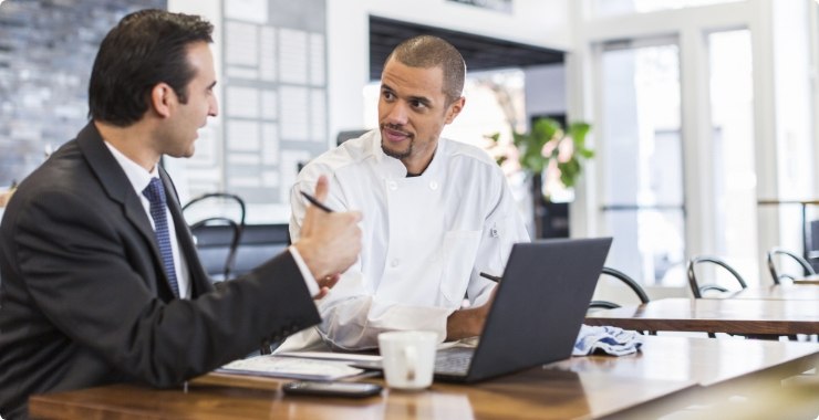 Business person and chef looking at a laptop in a restaurant setting