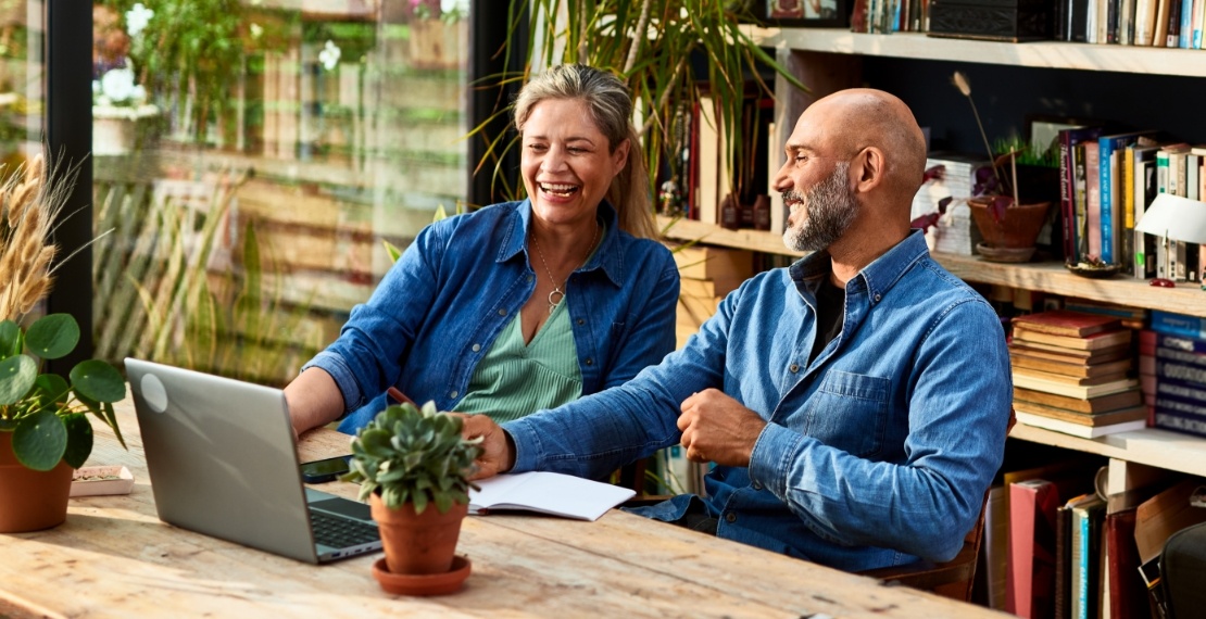 A man and a woman smile as they both look at a laptop.