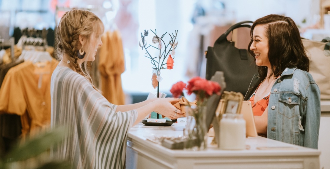 A female employee working in a clothing boutique interacts with a customer at the counter.