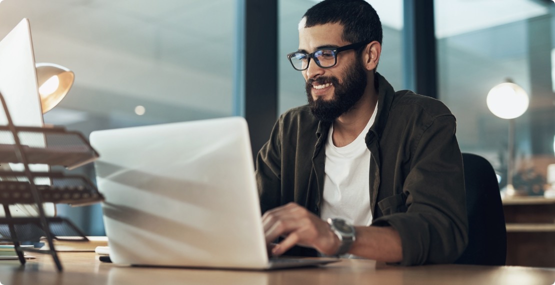A man types on his laptop while sitting at a desk.