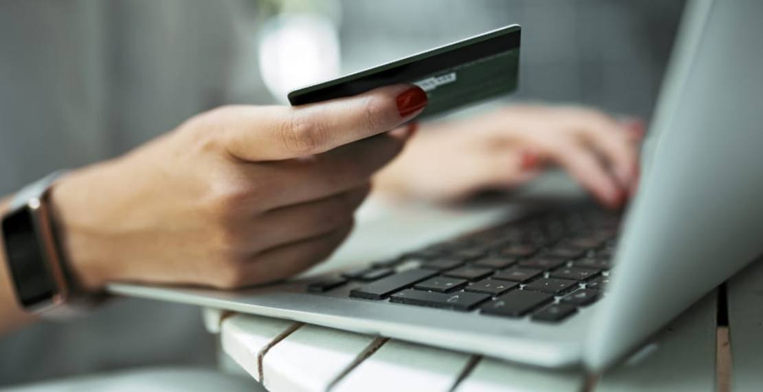 A woman holds a credit card in one hand while typing on a laptop with the other.