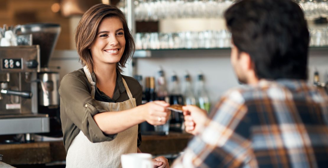 An image of a smiling bartender taking payment from a customer.