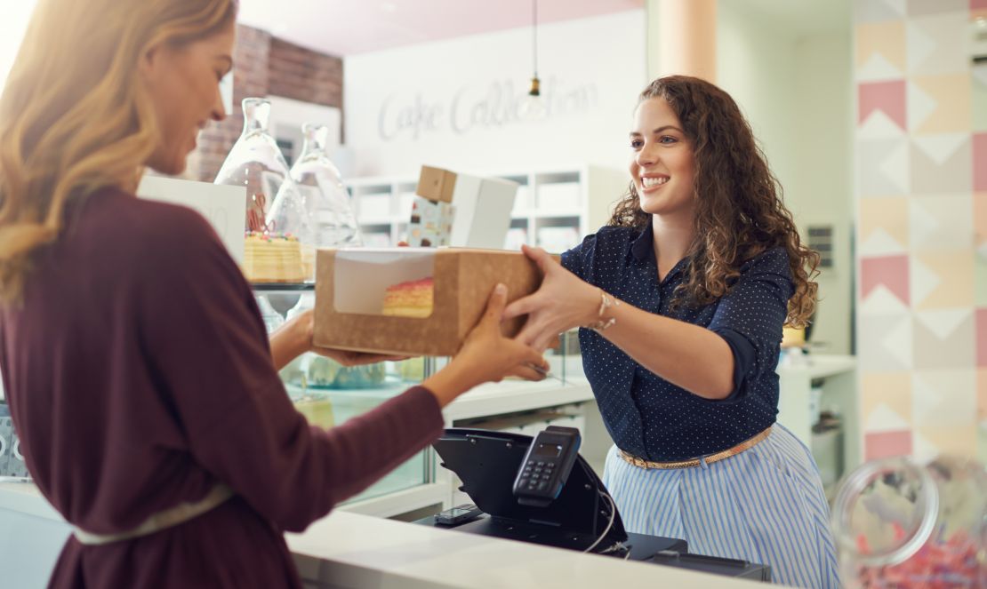 Bakery employee hands a boxed-up cake across the counter to a customer. 