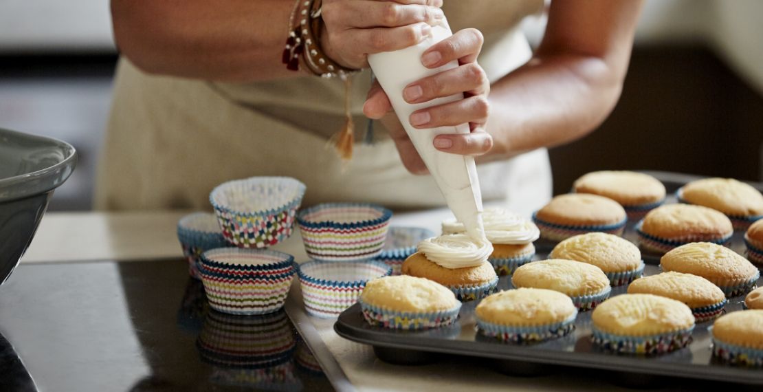 Person pipes icing onto a tray of cupcakes.