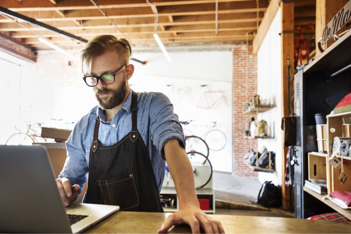 A coffee shop owner looks at a laptop in their business.