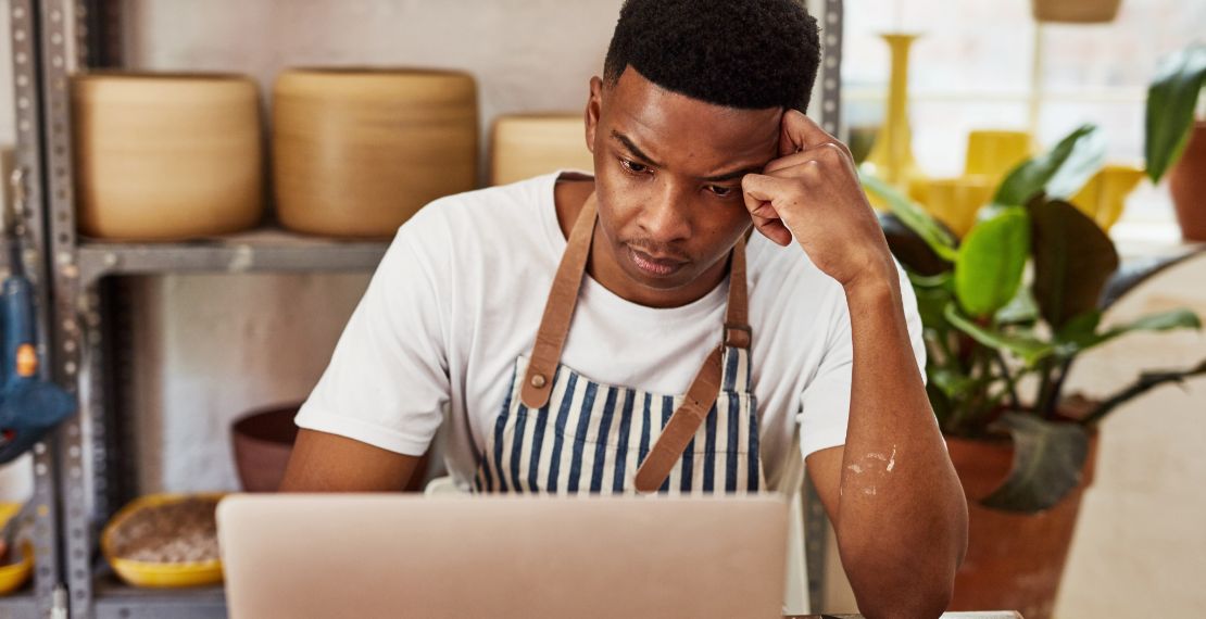 Person in blue and white striped apron looks at payment processing costs on laptop.