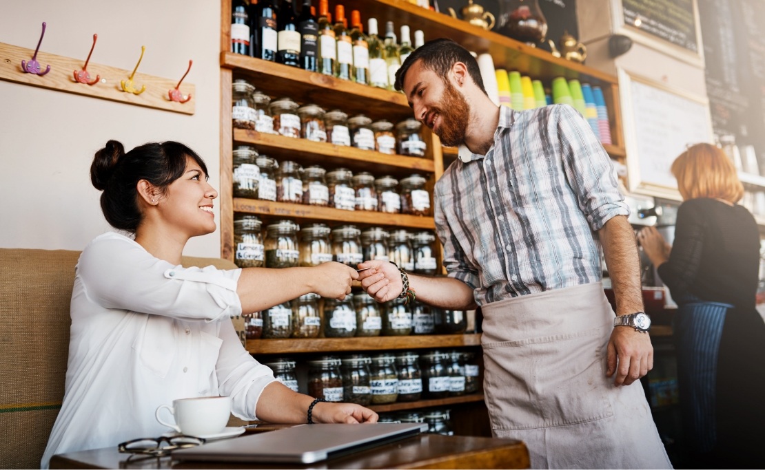 A female patron hands her payment to a male employee inside a restaurant. 