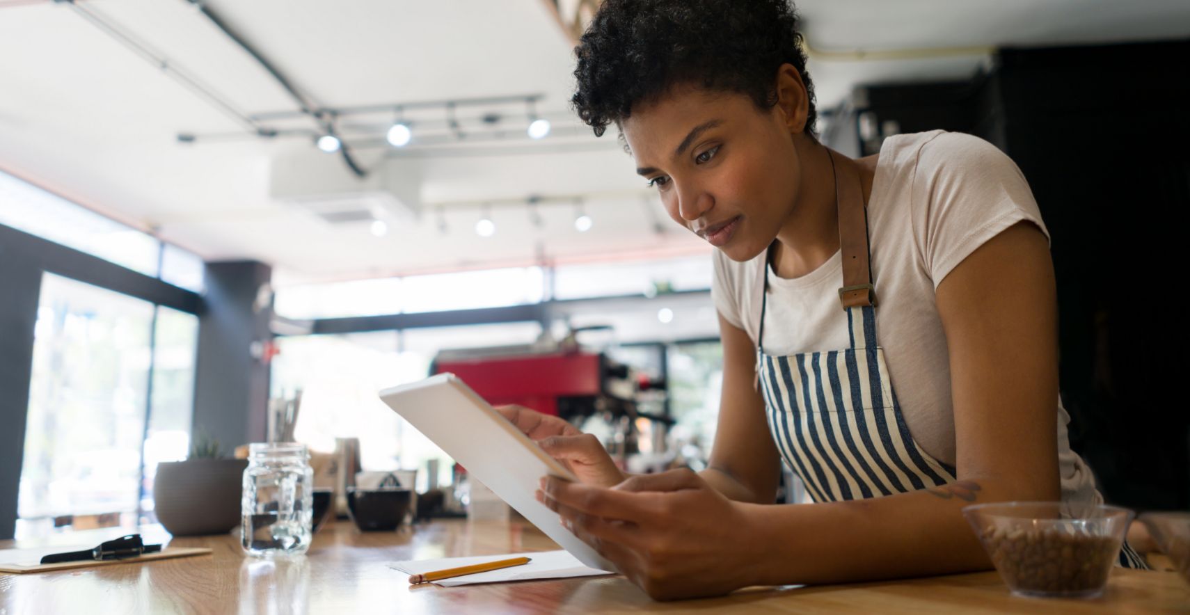 Female cafe employee looking down at a white mobile tablet at a counter