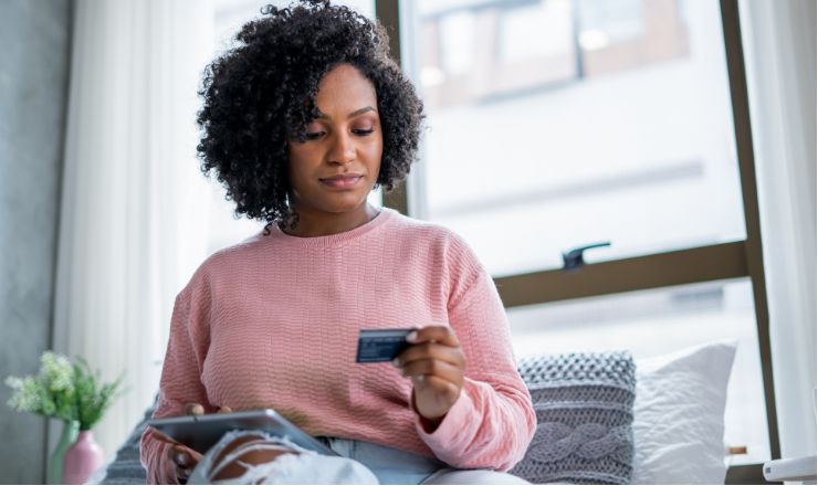 A woman holding a tablet and looking at a credit card in her other hand