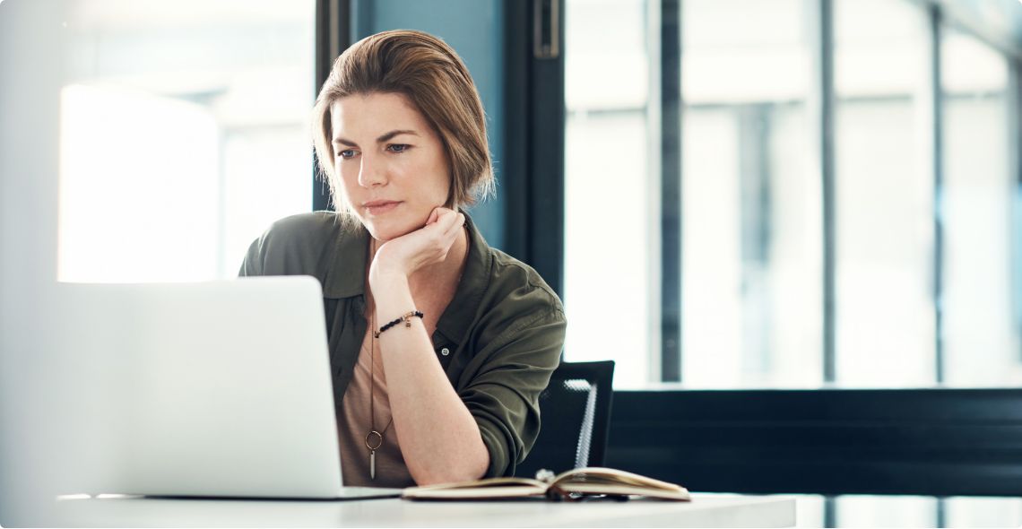 A woman leaning on her elbow as she looks at an open laptop