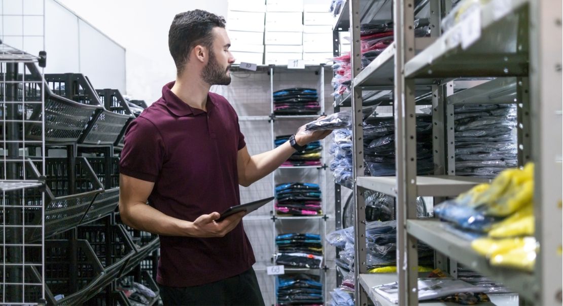 Man using a tablet to check clothing inventory in a stock room