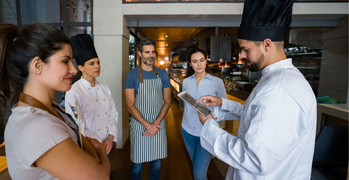 Chef looking down at an iPad restaurant POS and talking to four hotel restaurant staff members
