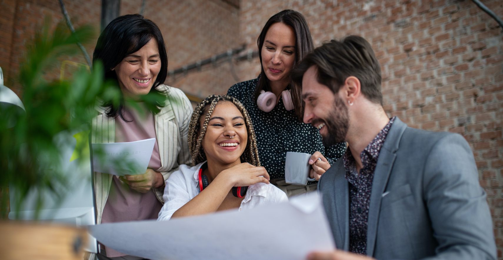 Group of four smiling employees gather around documents in an office and work together.