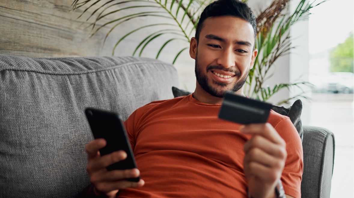 Man lying on couch, online shopping with his smartphone and credit card