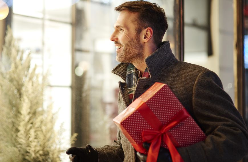 Man window shopping while holding a red wrapped Christmas gift