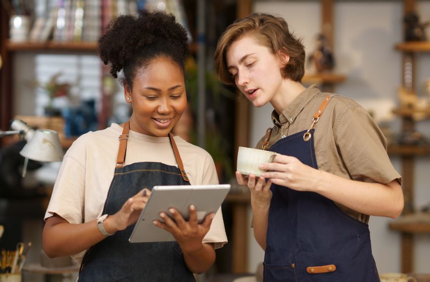 Two seasonal retail employees looking down at a mobile tablet POS