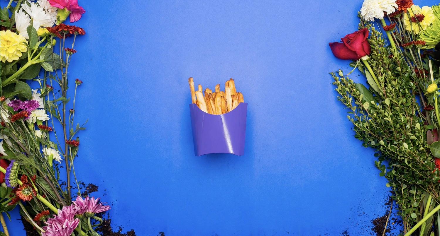 A box of french fries against a blue background with flowers laying along the edges