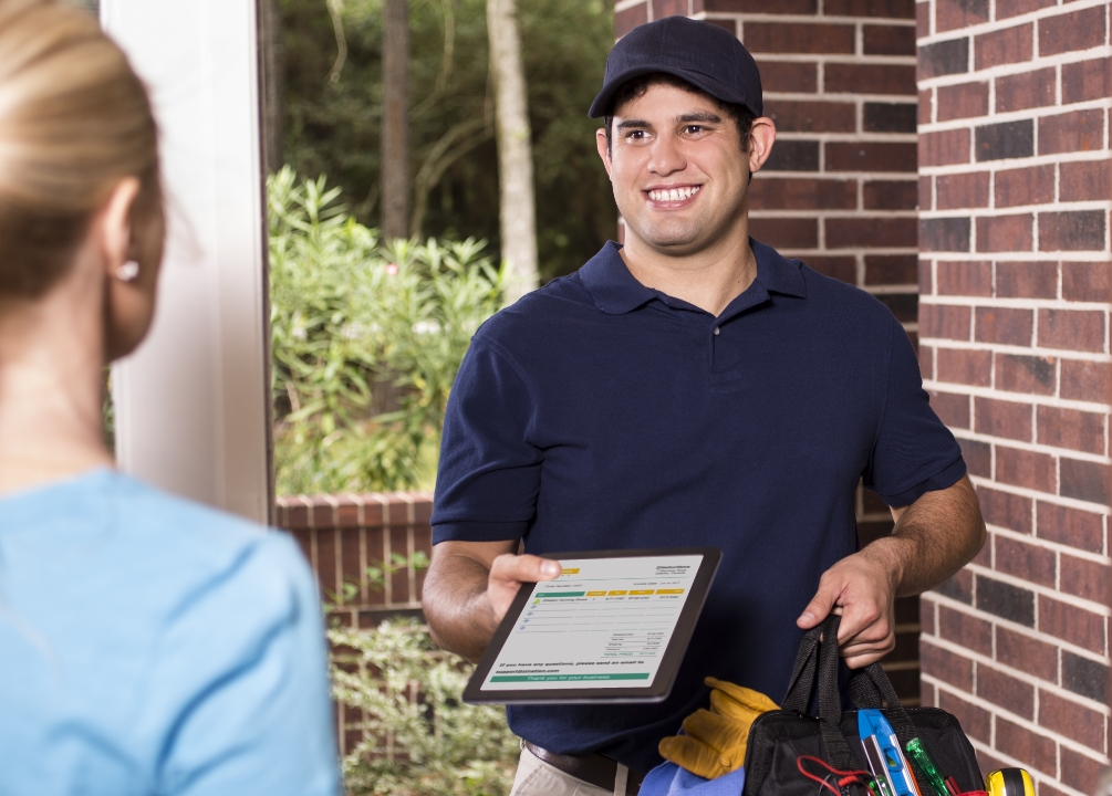 A home services employee standing at a door with a mobile pay device.