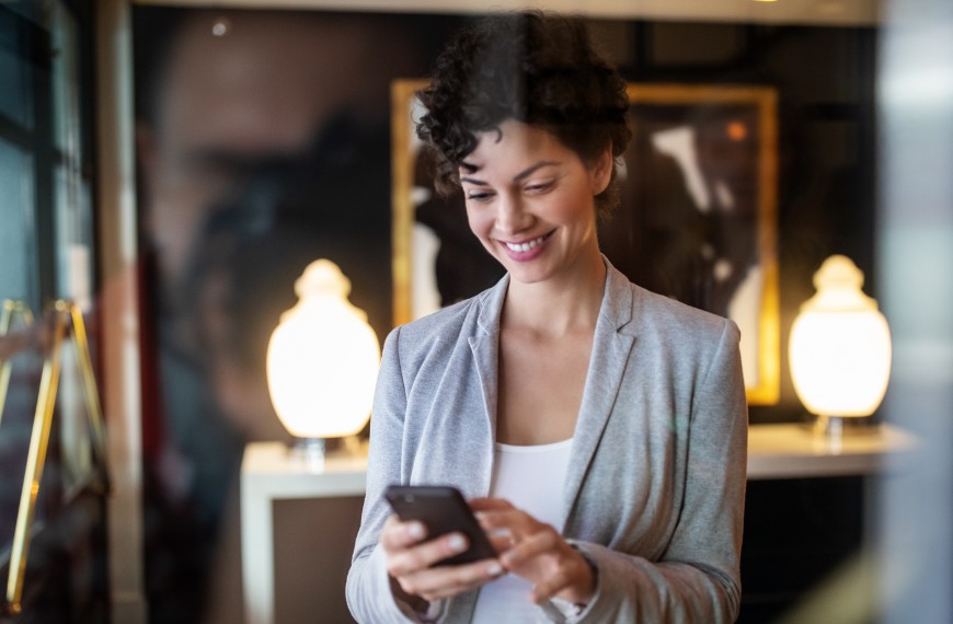 Woman in a gray blazer and white shirt smiles down at her phone as she views her customer loyalty rewards