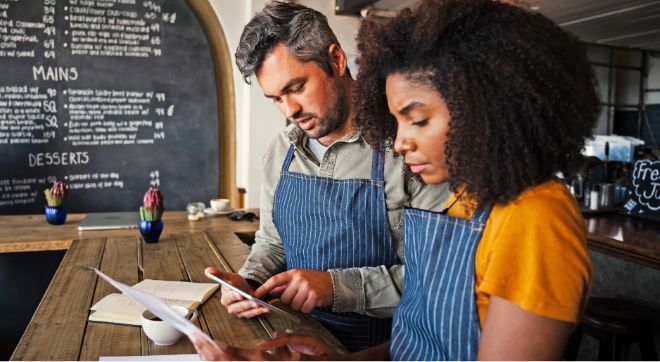 Man and woman behind a restaurant counter in aprons consider PCI-DSS documentation